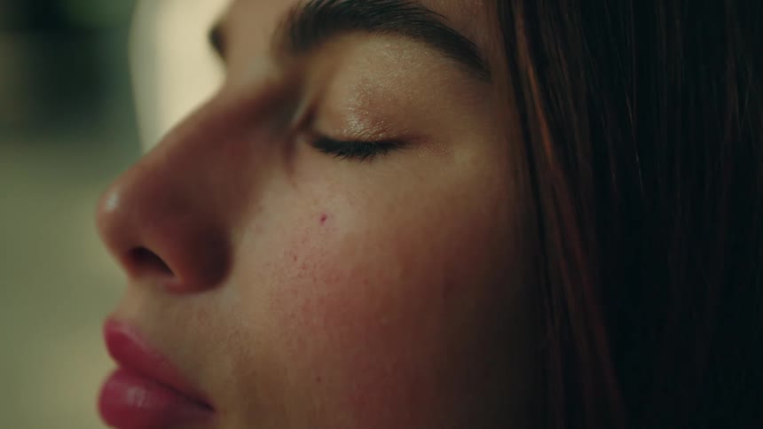 A woman with pink lipstick and dark hair keeps her eyes closed in a serene side profile