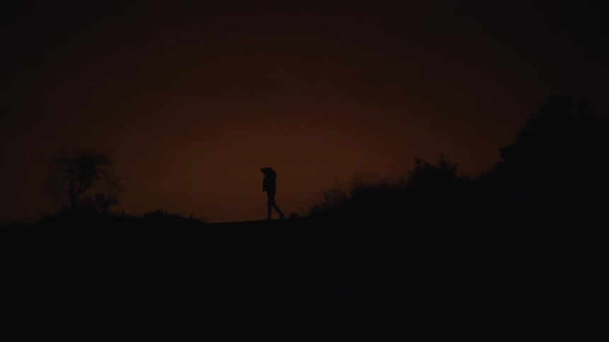 A silhouetted man paces outside at dusk