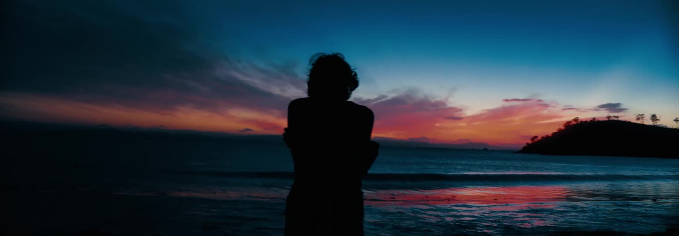 The woman watches the ocean at sunrise from the beach