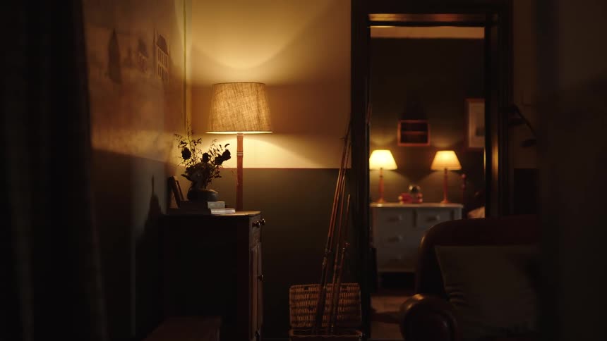 A view of a living room and an adjacent bedroom at night illuminated by several lamps with warm yellow light creating a cozy atmosphere