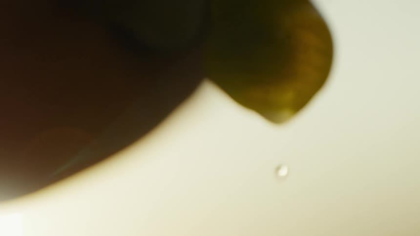 A close view of a translucent yellow grape as water drips from the bottom against a bright light