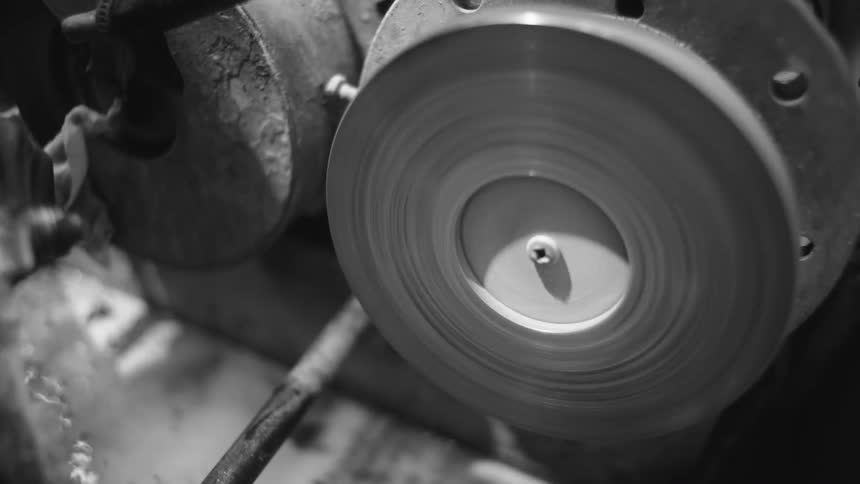 A black and white view of a rotating wheel being used to polish a piece of jewelry in a workshop