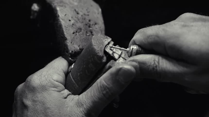 Hands manipulating a small metal mechanism attached to a stone block in a monochrome closeup