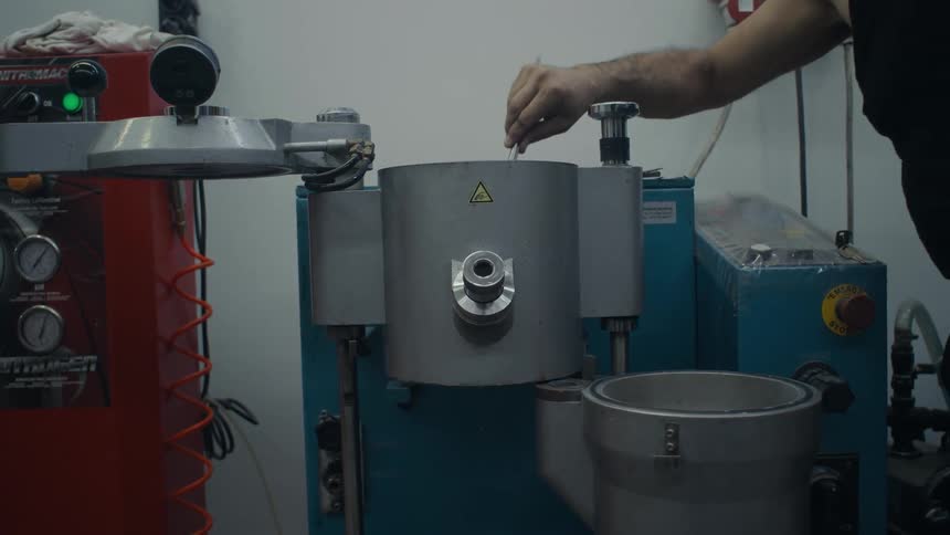 A person using a pair of long metal tweezers to carefully place or remove a small object from a large industrial machine in a workshop