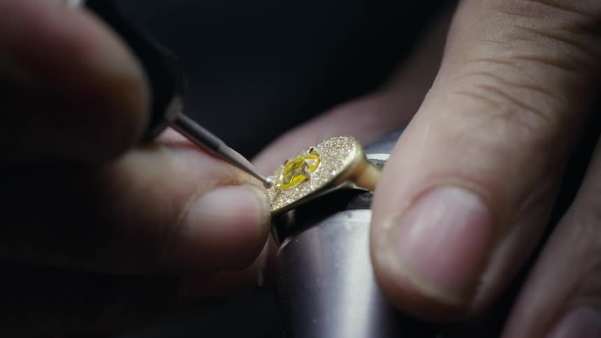 Hands of a jeweler working on a yellow diamond ring in a dark room