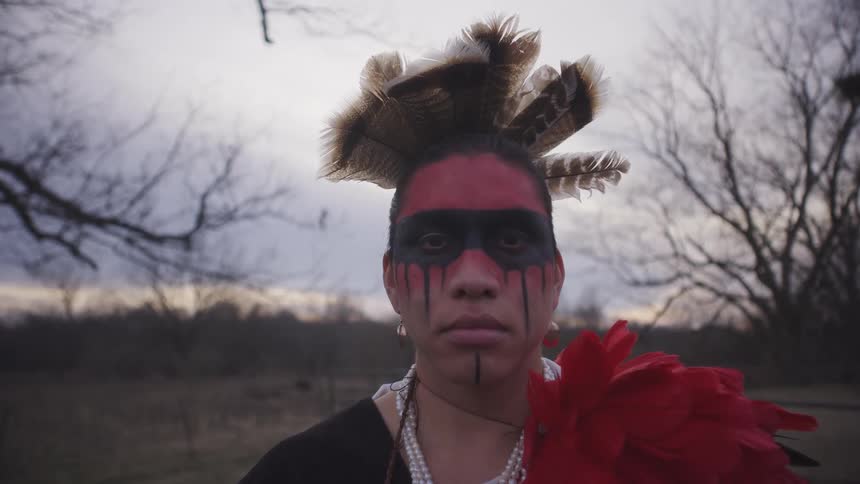 Man wearing feathers on his head and tribal makeup turns his head