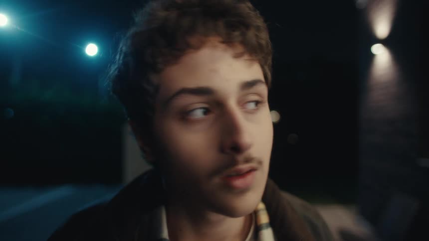 A young man stands outdoors awkwardly after an interrupted romantic moment at night