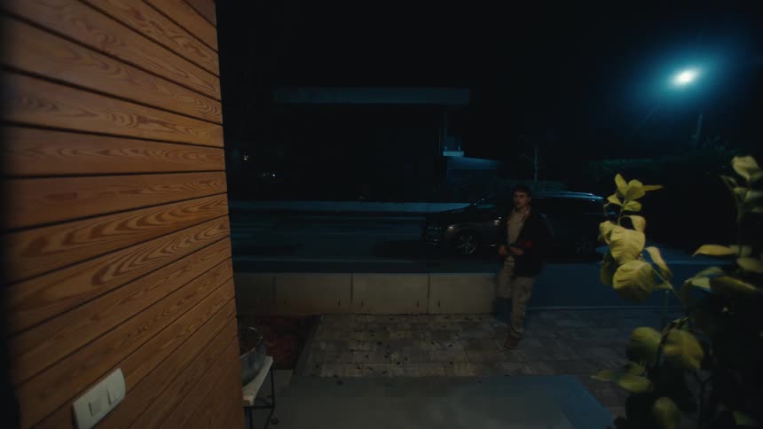 Man holding red flowers in front of a residential entrance at night with artificial lighting around