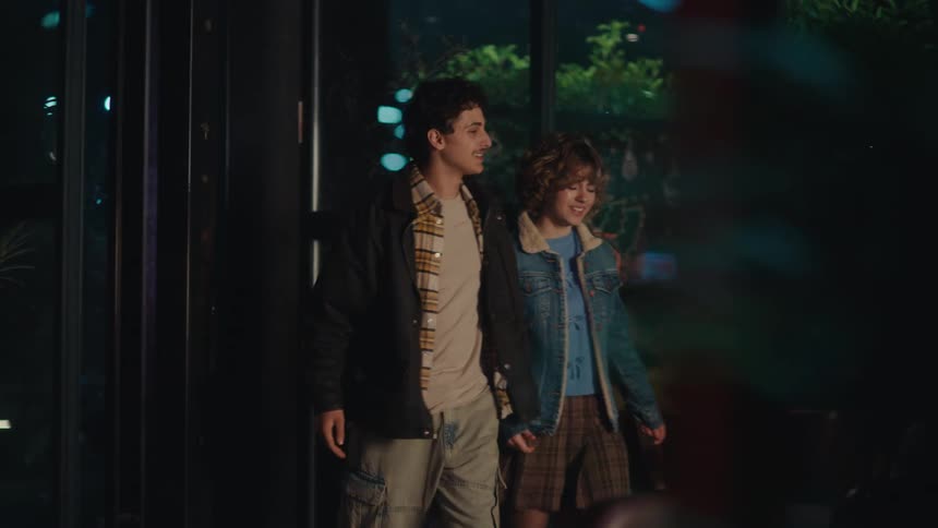 Couple entering a restaurant at night walking side by side in front of an illuminated glass facade