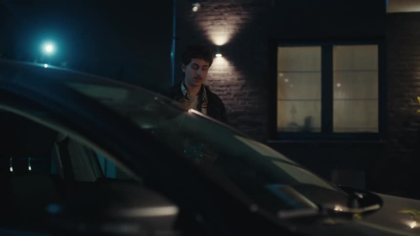 A man getting out of a car and walking up to a door on a house carrying a rose