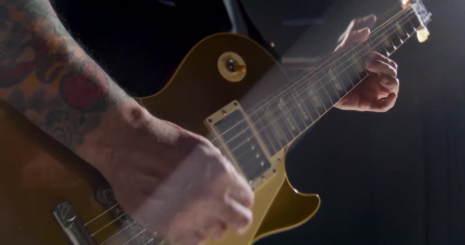 Hands play a gold electric guitar under studio lighting