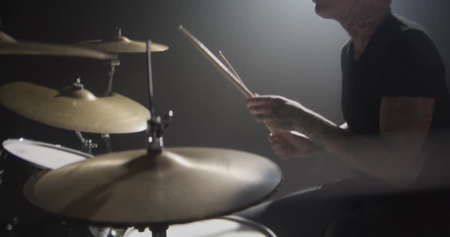 The man hits the drums while sitting under the spotlight