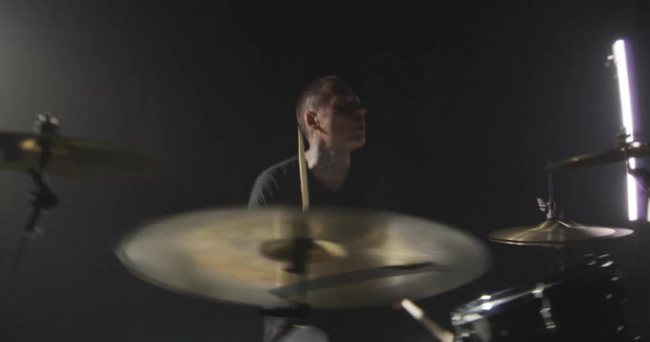 Drummer playing in a dark environment with directional lighting and a partially visible drum kit