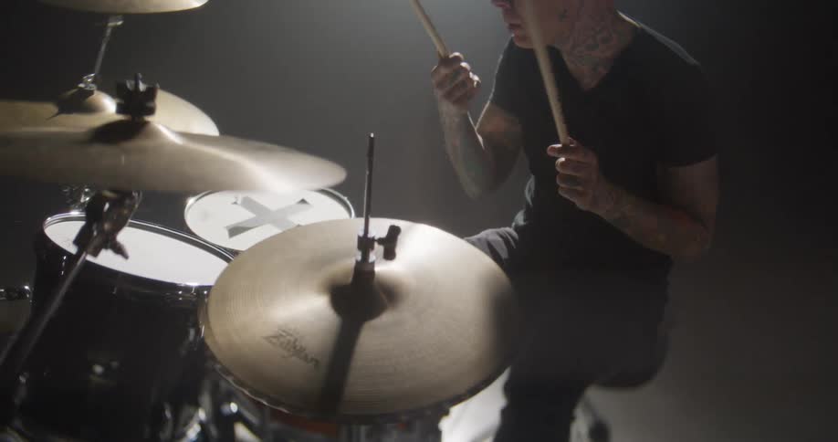 The man is playing the drums under a spotlight