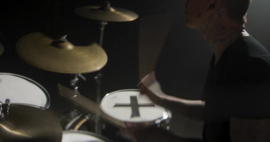 A drummer playing a drum kit under dramatic stage lighting in a dark studio