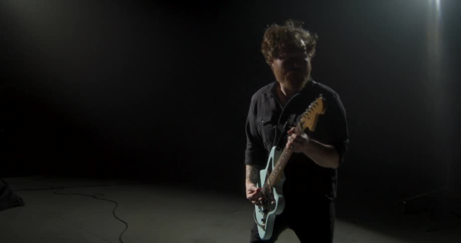Guitarist plays an electric guitar in a studio with dramatic lighting