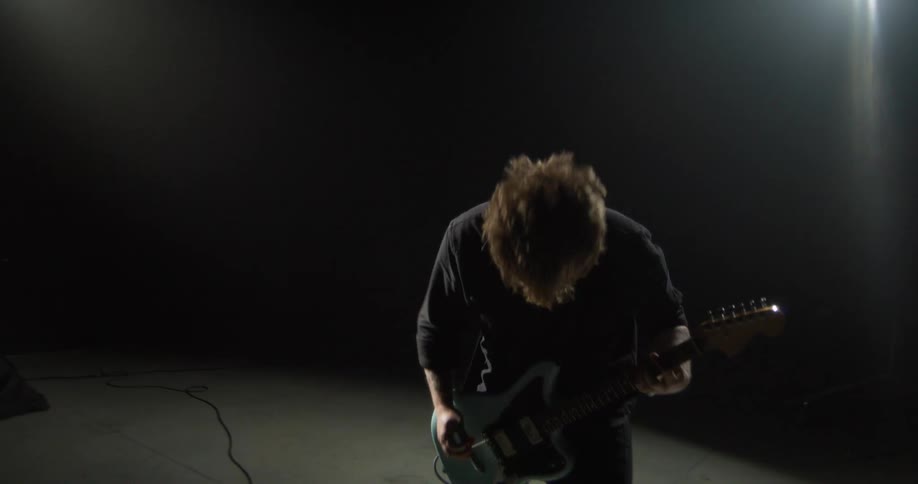 Guitarist playing in a dark studio with directional lighting and a cable connected to the instrument