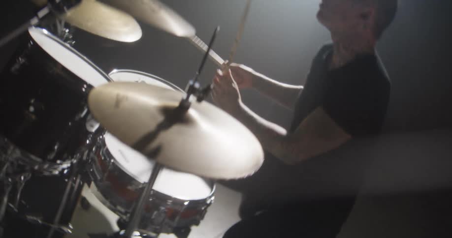 Adult man wearing dark clothes playing drums indoors