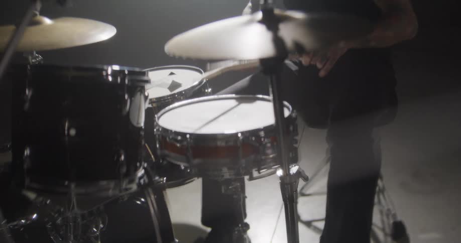 Adult man wearing dark clothes playing a snare drum on a drum set indoors