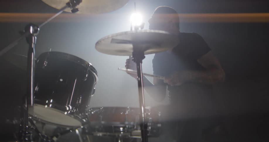 Drummer plays cymbal and snare in a studio with focused lighting