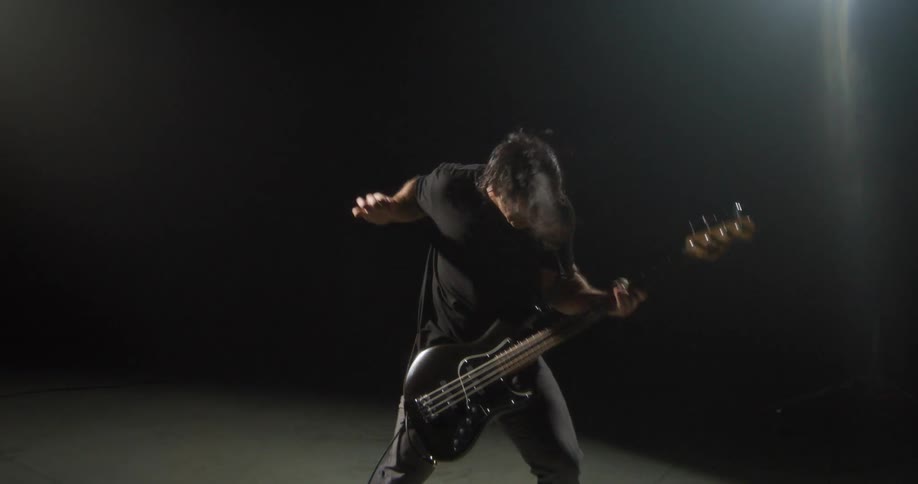 Young adult man wearing black clothes playing an electric bass guitar indoors