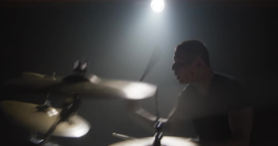 A drummer plays a drum kit on a dark concert stage during a live performance