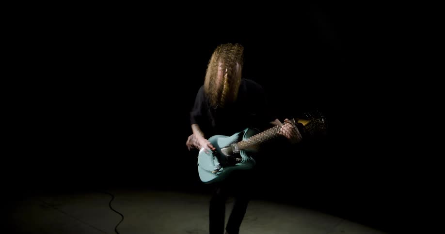 Guitarist playing in a dark studio with directional lighting and motion blur on the instrument