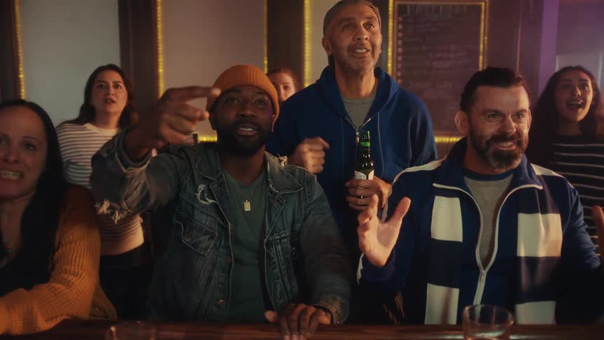 A group of diverse friends watches a sports game at a bar their faces filled with intense anticipation and nervous energyas the play concludes the tension breaks into a joyous celebration with the group cheering clapping and raising their hands in