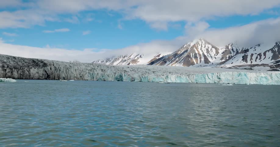 Extensive glacier beside the sea with snowcovered mountains in the background under a partly cloudy sky