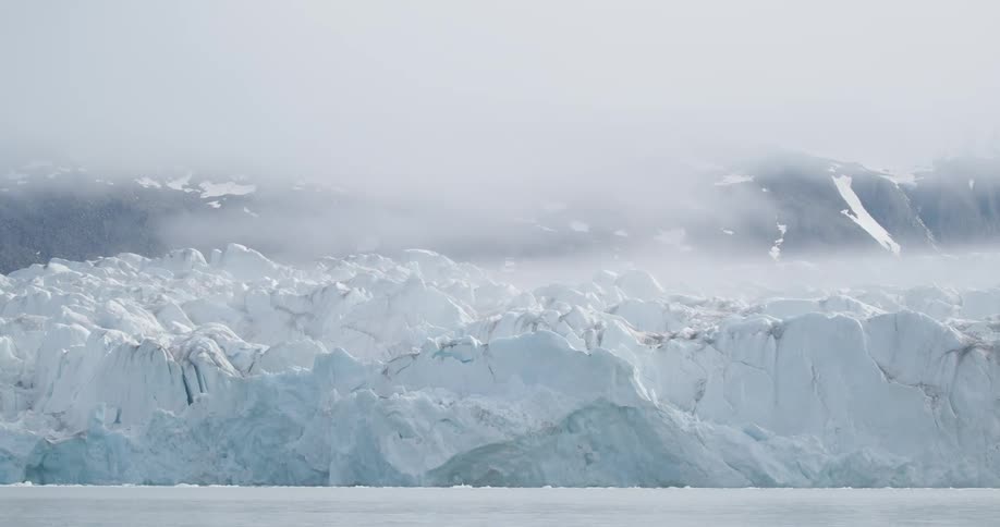 An iceberg floating on the arctic sea with fog drifting through the air and softening the atmosphere