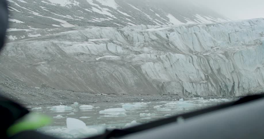 Gray glacier with visible fractures above a lake with floating ice fragments