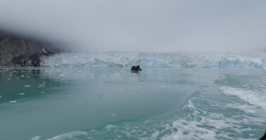 A small boat filled with passengers navigates through icy waters toward a massive fogcovered glacierthe scene captures the vast scale of the arctic landscape with chunks of ice floating in the turquoise sea