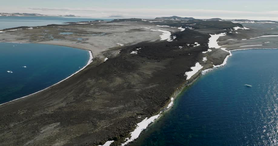 Rocky peninsula between two bluewater bays with patches of snow scattered across the terrain