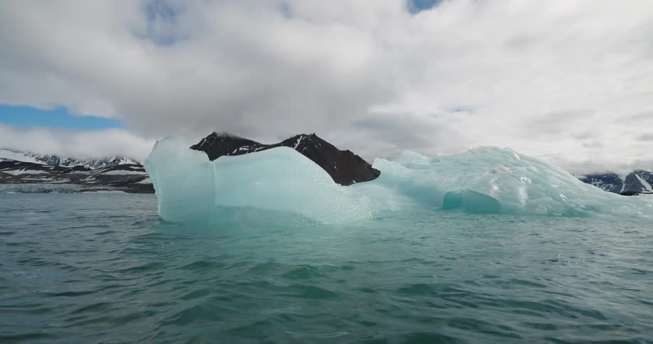Blue ice blocks floating in cold water with dark partially snowcovered mountains in the background
