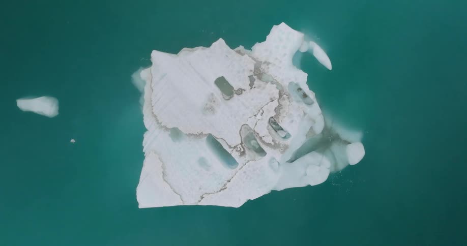 Floating ice floe with visible cracks and cavities in bluegreen waters