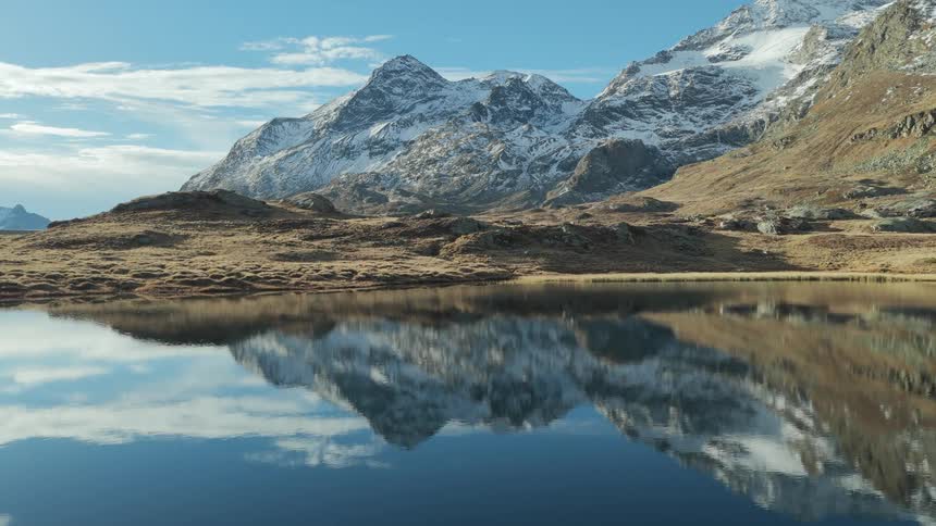 Still lake water reflects the nearby mountain in winter some of them snow dusted on a cloudy day
