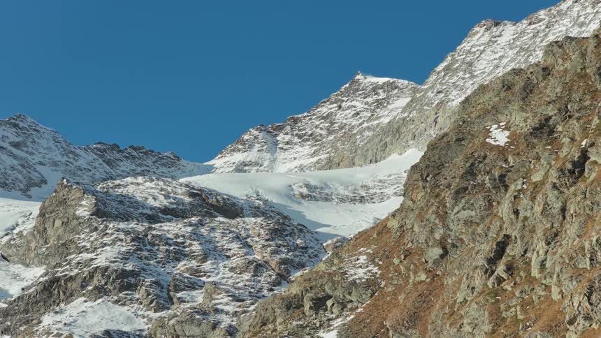 Snowcovered mountain peaks rise above rocky slopes under a clear blue sky