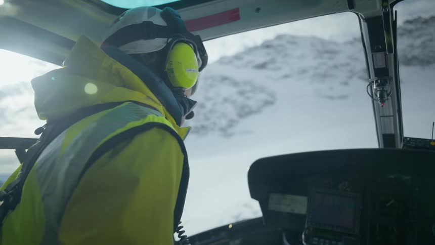 Helicopter crew member looks at a snowy mountain landscape from the cockpit