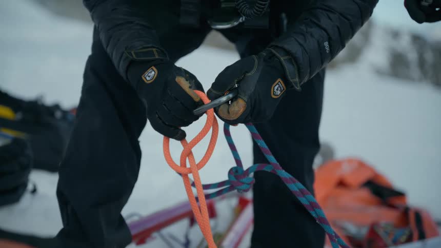 This line is a vibrant solid orange color it appears to be a dynamic climbing rope with a smooth braided sheath it is the primary focus of the action as the individual threads it through a metal carabiner to create a loop or knot