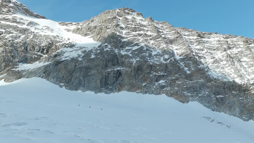 Rocky mountain covered with snow with small climbers crossing the icy field
