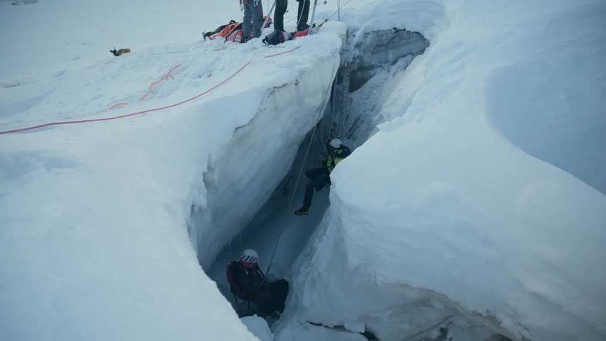 Rescue team operates inside a deep glacier crevasse using a rope system