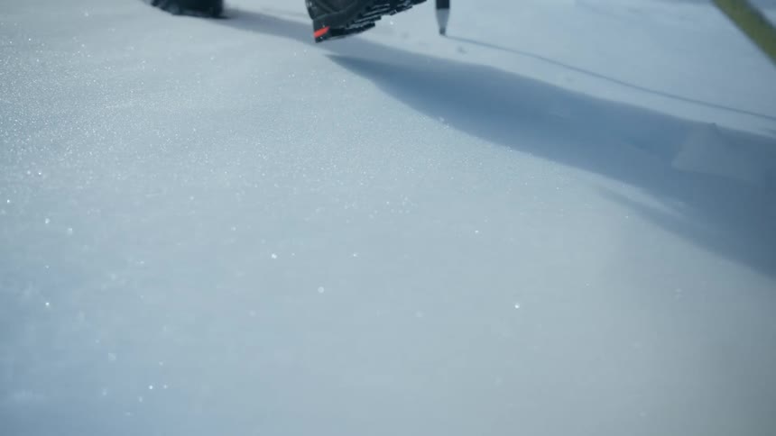 A thick yellow climbing rope rests on a bright glistening field of snow as the camera moves a mountaineer wearing yellow pants and dark hiking boots treks through the deep powder leaving a trail of footprints behind
