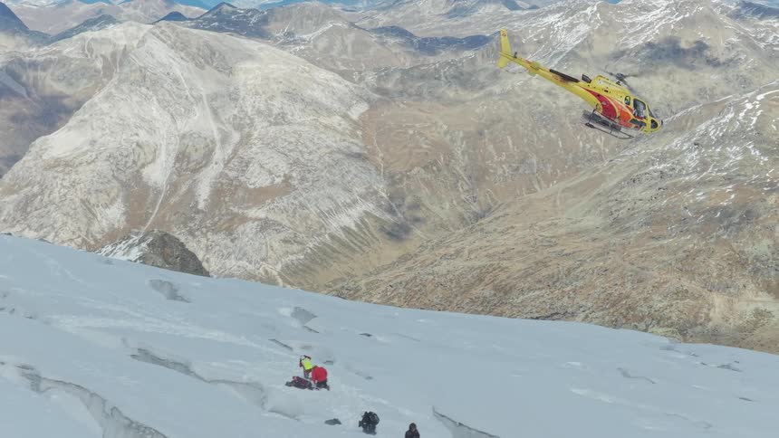 Rescue helicopter hovers above a glacier as a team waits on a snowy slope