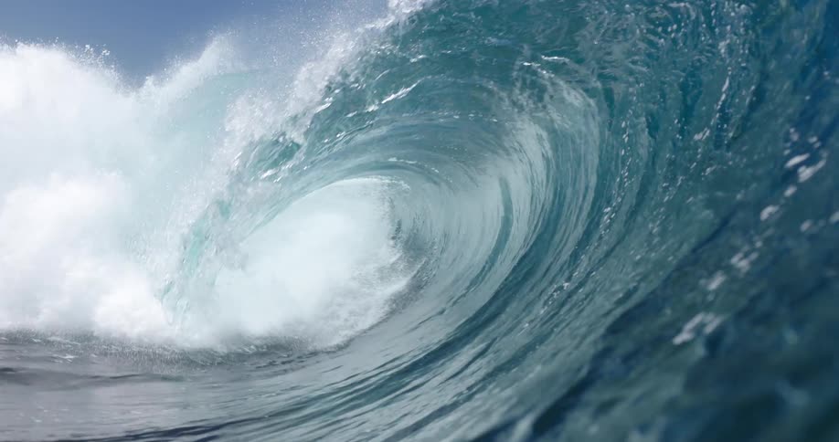 A large ocean wave curls into a powerful barrel under a clear blue sky before the camera moves inside the tube and becomes submerged in churning water and white foam