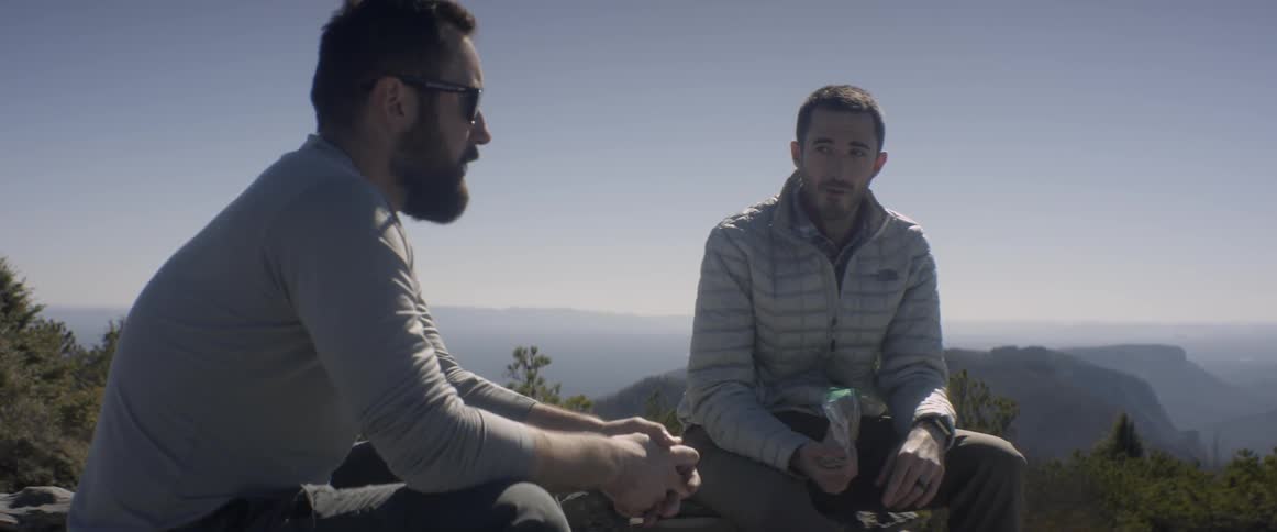 Two men talk sitting on a mountain