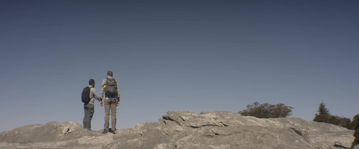 Two men stand on a rocky hill on a clear day