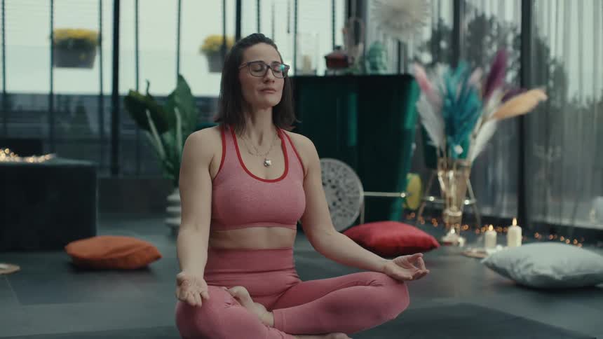 A woman meditates cross legged while holding a singing bowl in a serene indoor studio