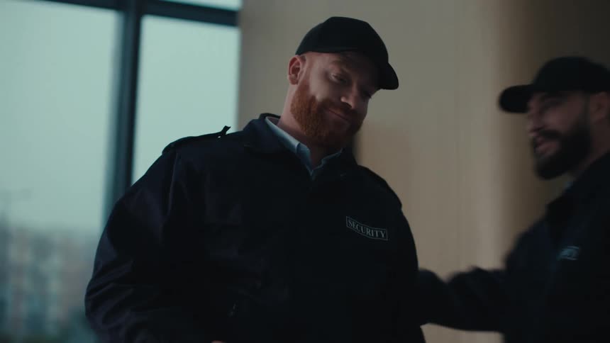 Two security guards greet each other during a shift change inside a modern security office