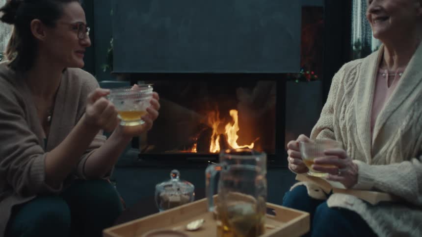 Mother and daughter sit together having a conversation while sharing tea by a cozy fireplace