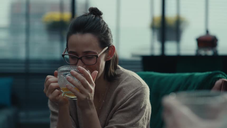 Woman holds her cup with both hands and smells her tea as she drinks tea with a friend